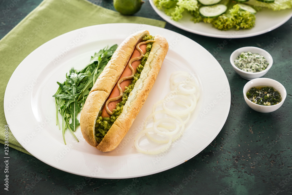 Plate with tasty hot dog on color table Plate with tasty hot dog on color table