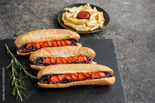 Slate plate with tasty hot dogs on dark table