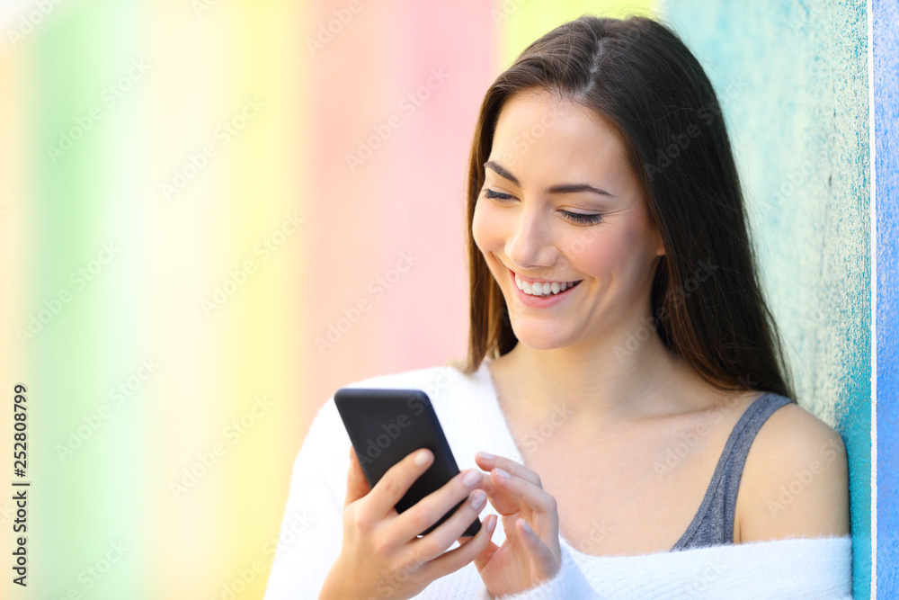 Happy woman is browsing smart phone beside a colorful wall Happy woman is browsing smart phone beside a colorful wall
