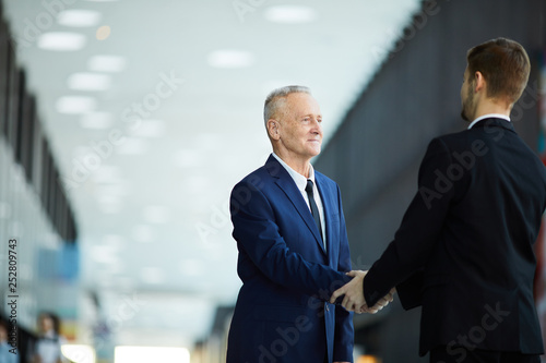 Waist up portrait of successful senior businessman shaking hands with partner standing in hall of business center, copy space