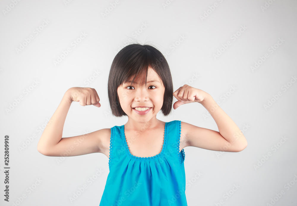 Strong little girl showing muscles on gray background Strong little girl showing muscles on gray background