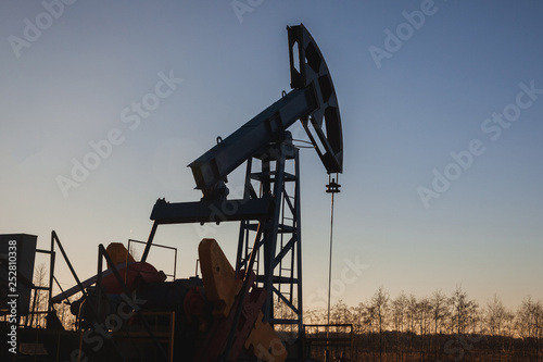 Oil pump on the background of blue sky and the morning sun, sun glare on the oil pump