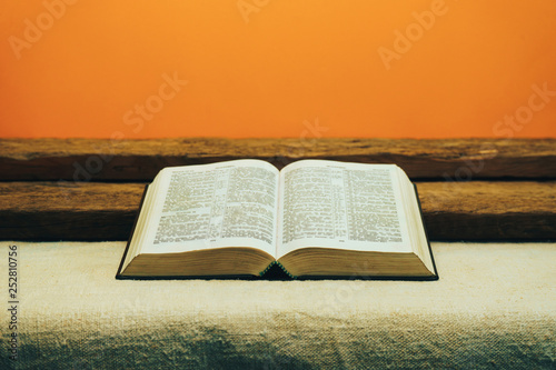 Open Bible on a old table. Beautiful yellow wall background. Religion concept. photo