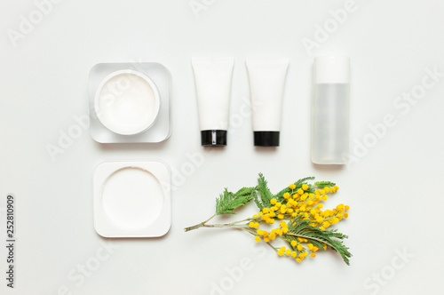 White cosmetic bottle containers with yellow Mimosa flowers on light background top view flat lay. Cosmetics SPA branding mock-up  Natural organic beauty product concept  Minimalism cosmetics style