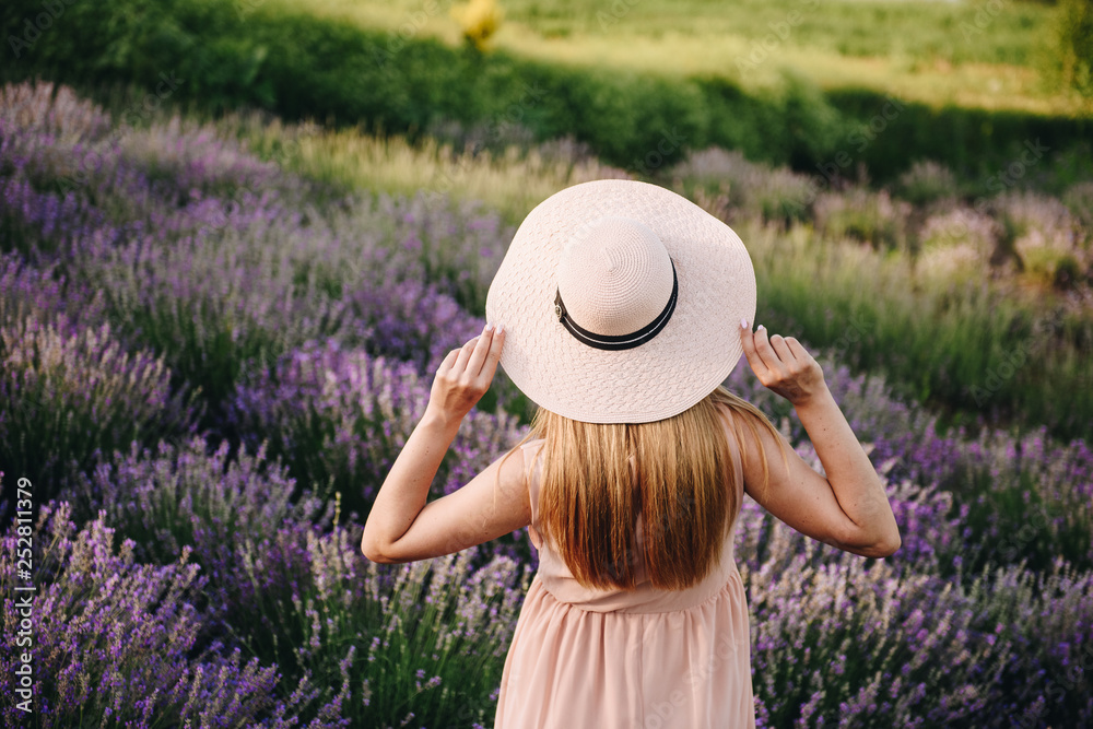 Fototapeta premium Pregnant girl blonde in a beige dress and straw hat. Lavender field. In anticipation of a child. The idea of a photo shoot. Walk at sunset. Future mom.