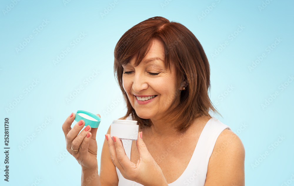 beauty, skincare and cosmetics concept - smiling senior woman with cream jar over blue background beauty, skincare and cosmetics concept - smiling senior woman with cream jar over blue background