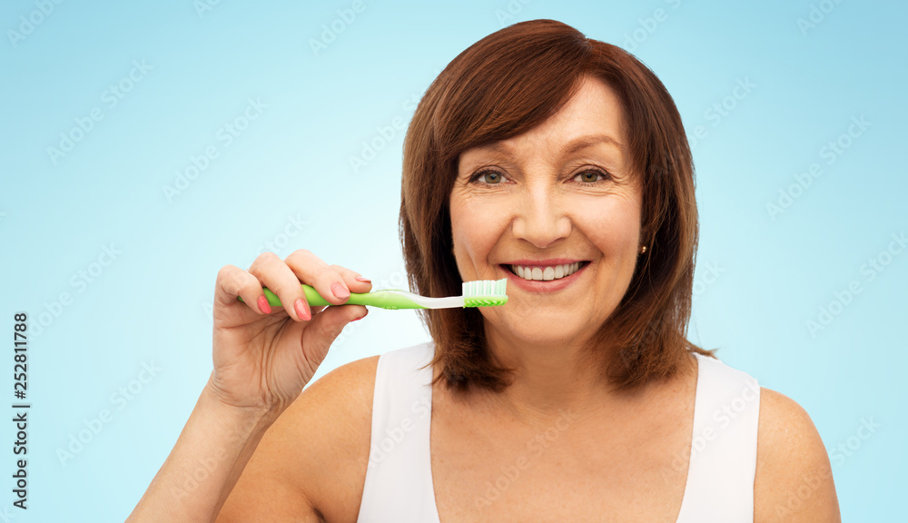 dental care and hygiene people concept - portrait of smiling senior woman with toothbrush brushing her teeth over blue background dental care and hygiene people concept - portrait of smiling senior woman with toothbrush brushing her teeth over blue background