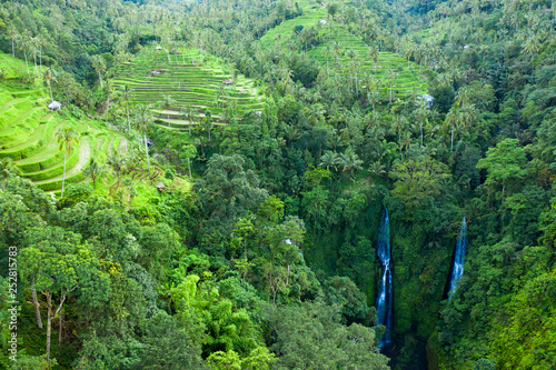 Aerial over Sekumpul waterfall surrounded by dense rainforest and mountains shrouded in mist at sunrise, Bali, Indonesia
