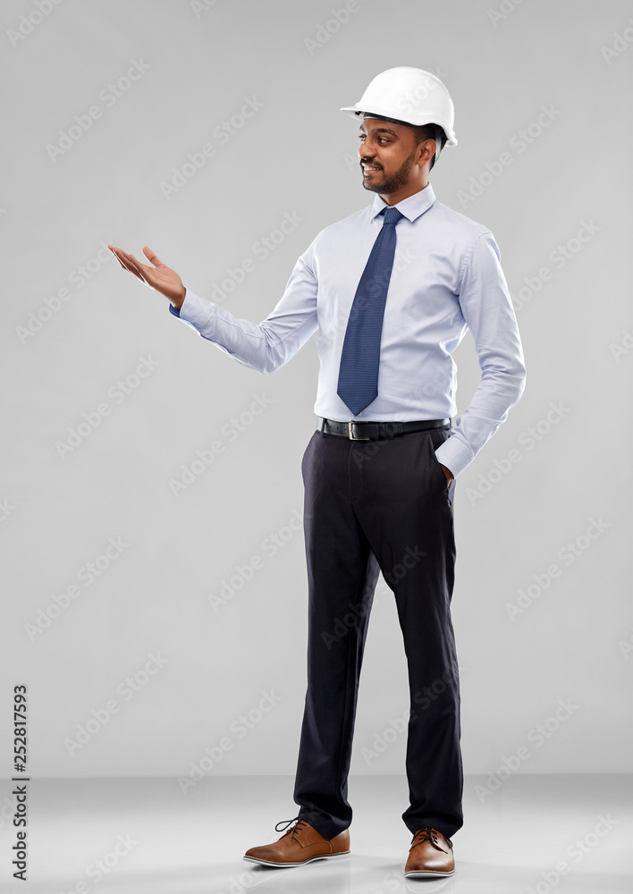 architecture, construction business and building - smiling indian architect or businessman in helmet showing something imaginary over grey background architecture, construction business and building - smiling indian architect or businessman in helmet showing something imaginary over grey background