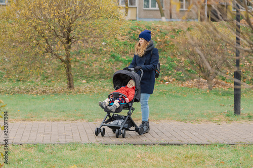 A woman walks in the park with a stroller and a small child.