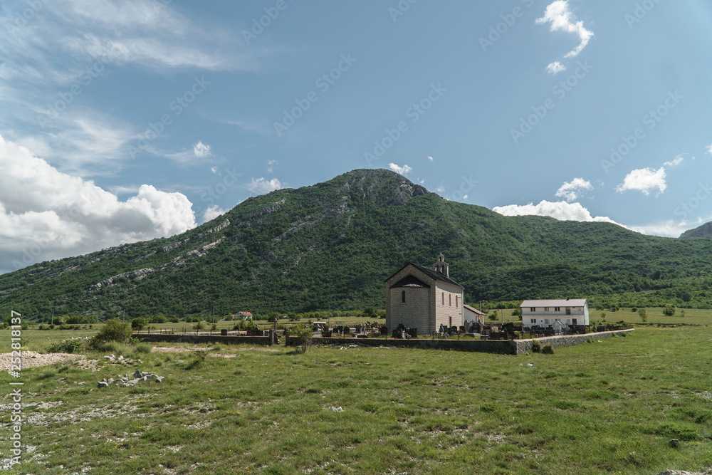 Old church with a cemetery in the middle of a green meadow with a mountain in the background
