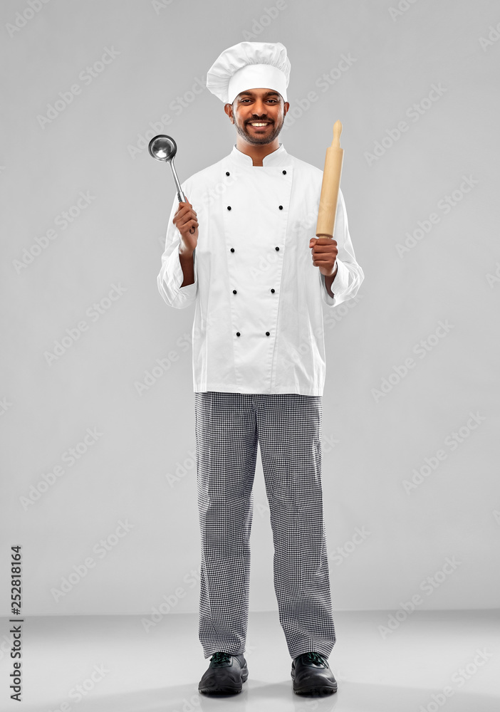 cooking, profession and people concept - happy male indian chef in toque with ladle and rolling-pin over grey background cooking, profession and people concept - happy male indian chef in toque with ladle and rolling-pin over grey background