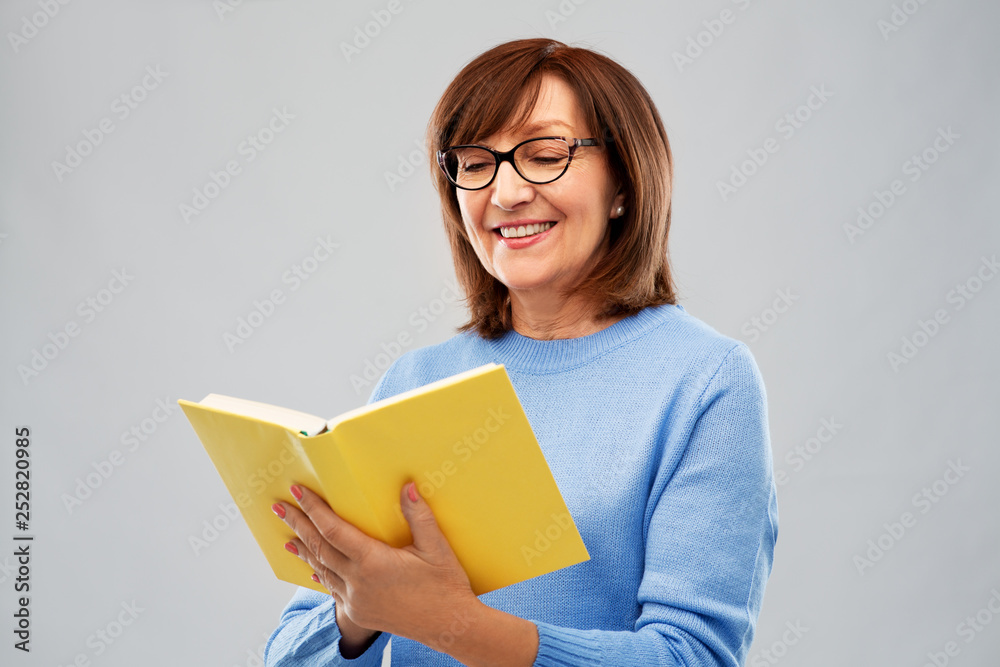 vision, wisdom and old people concept - portrait of smiling senior woman in glasses reading book over grey background vision, wisdom and old people concept - portrait of smiling senior woman in glasses reading book over grey background