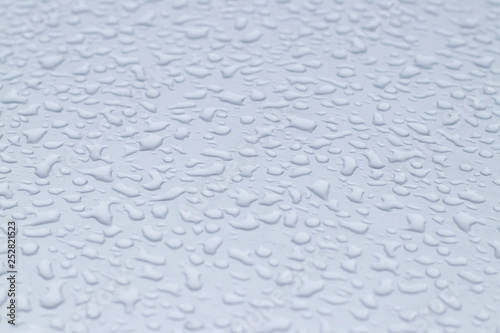 View of the big raindrops on the roof of a light blue car