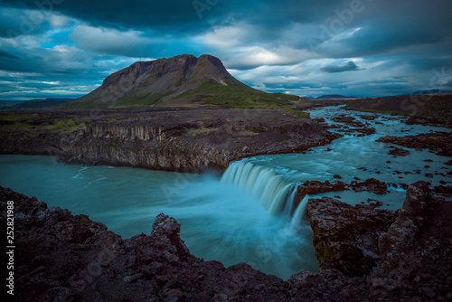 The Bjófafoss Waterfall with golden clouds in the sky. The flowing water is captured by a long exposure. Amazing blue color of water from the glacier. Natural and colorful environment...