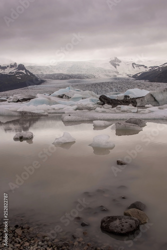 The Fjallsarlon is a large glacial lake in southeast Iceland, the floating ice floes on a quiet surface of gracial lagoon, a dramatic sunset sky is reflected on the surface