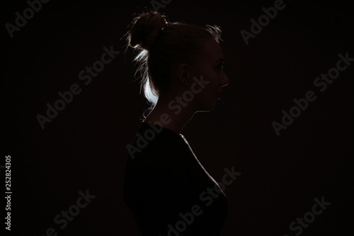 Φωτογραφία profle view of woman hiding in the dark to preserve anonymity - backlit contour