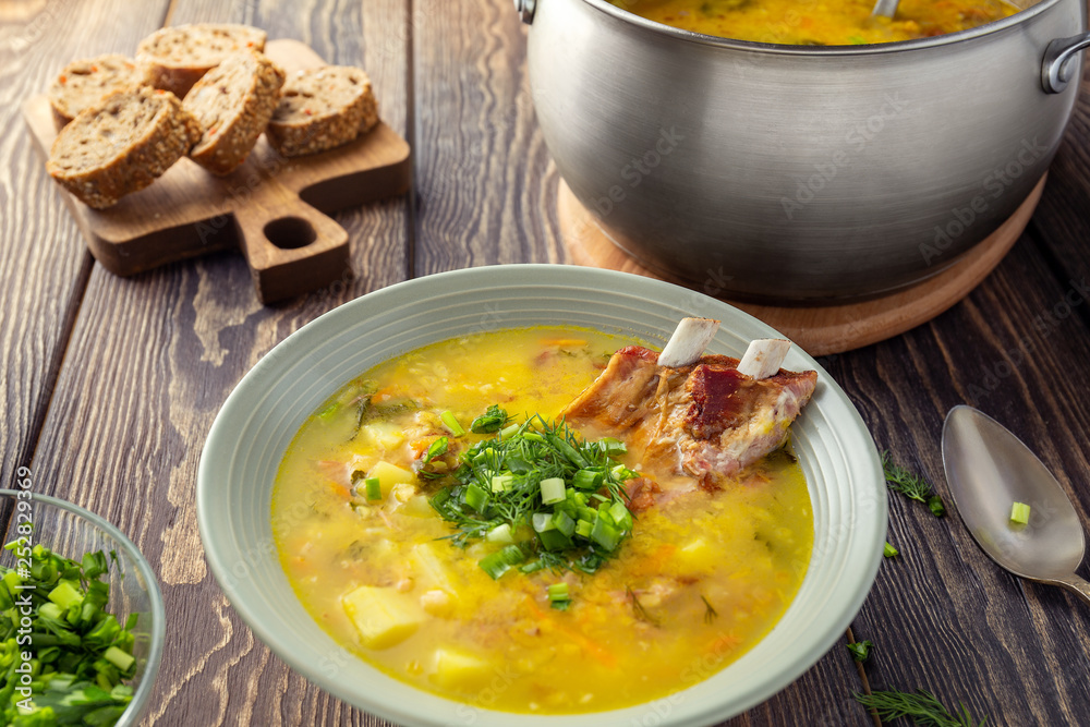Fragrant yellow split pea soup with smoked pork ribs on a wooden table. Fragrant yellow split pea soup with smoked pork ribs on a wooden table.