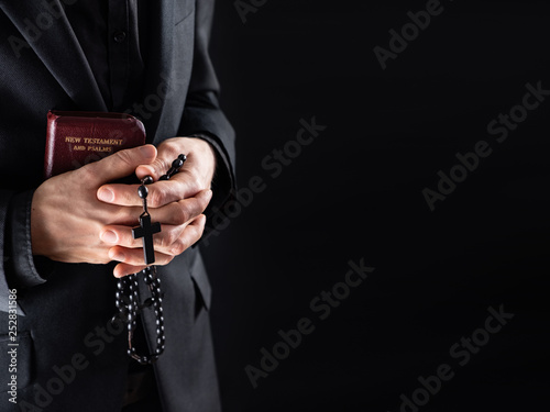 Hands of a christian priest dressed in black holding a crucifix and New Testament book Fototapet