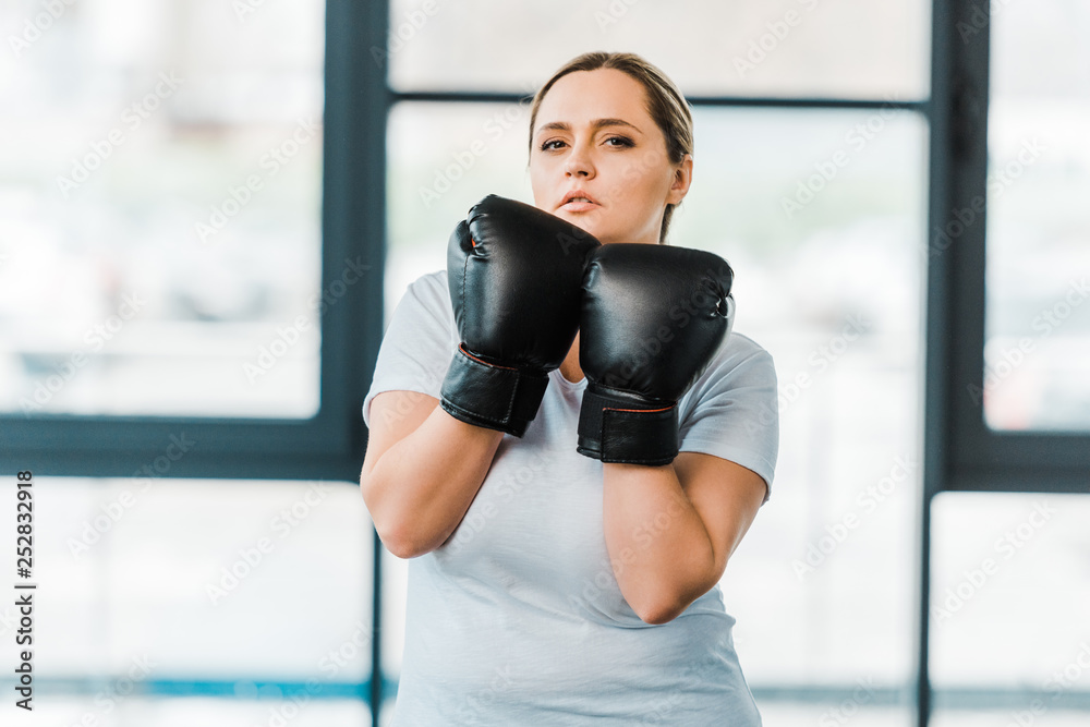 serious overweight girl standing in boxing gloves in gym