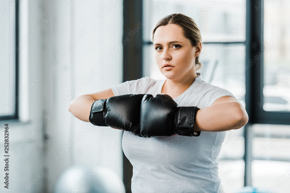 confident overweight girl standing in boxing gloves while practicing kickboxing