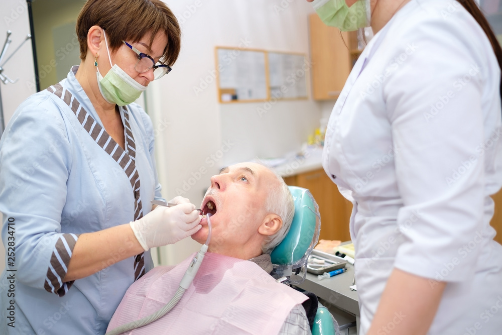 Dentist and nurse making professional teeth cleaning male senior patient at the dental office. Dental care for older people. Dentistry, medicine and health care concept