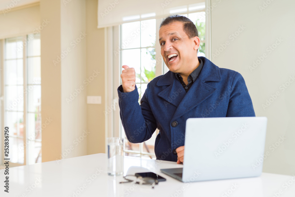 Middle age business man working using laptop smiling with happy face looking and pointing to the side with thumb up.