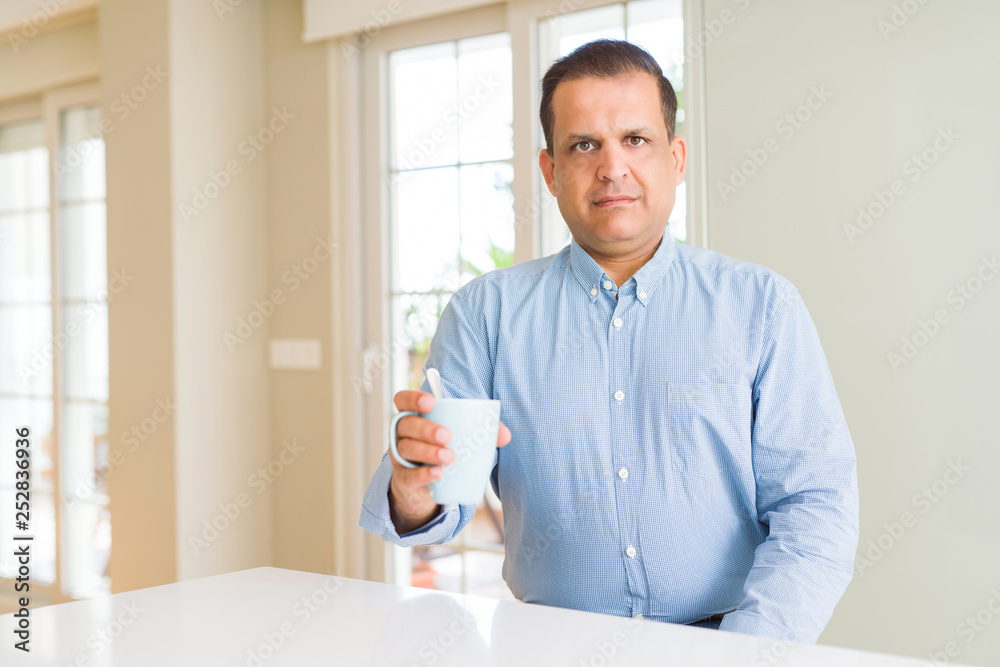 Middle age man drinking coffee in the morning at home with a confident expression on smart face thinking serious