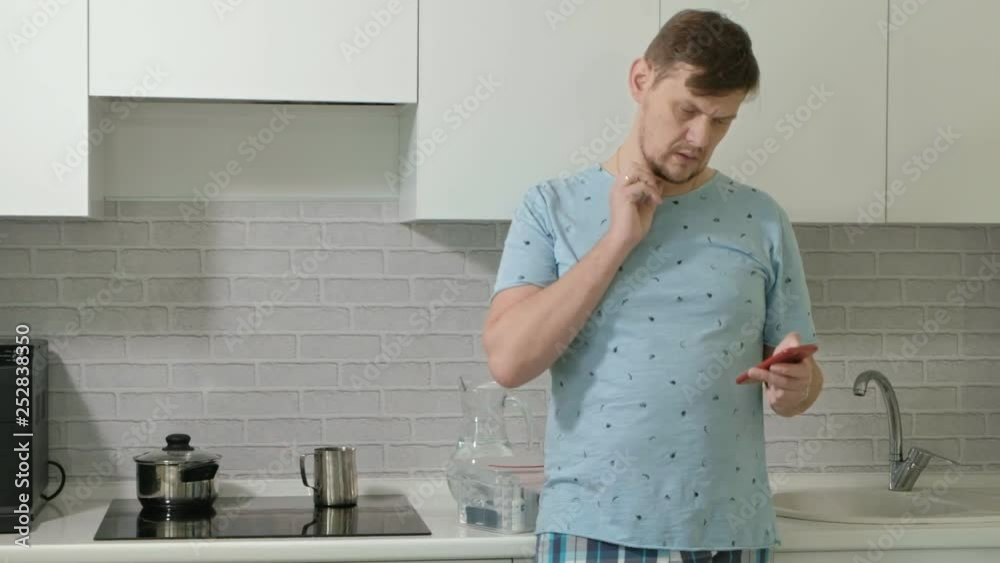 A man in pajamas drinking water in the kitchen. Morning A man in pajamas drinking water in the kitchen. Morning