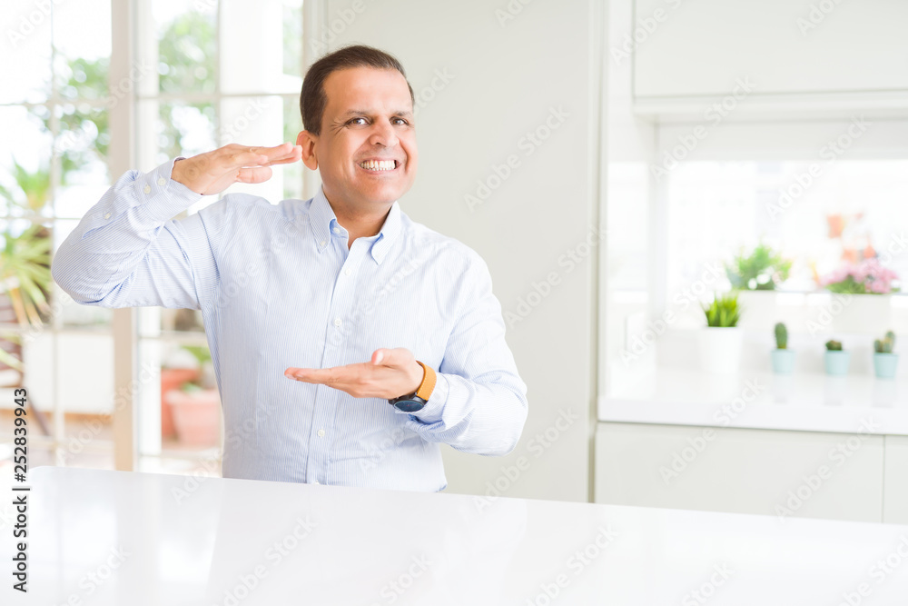 Middle age man sitting at home gesturing with hands showing big and large size sign, measure symbol. Smiling looking at the camera. Measuring concept. Middle age man sitting at home gesturing with hands showing big and large size sign, measure symbol. Smiling looking at the camera. Measuring concept.