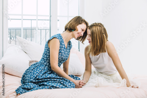 Mother and daughter girl child sitting happy and smiling at home in bedroom on bed