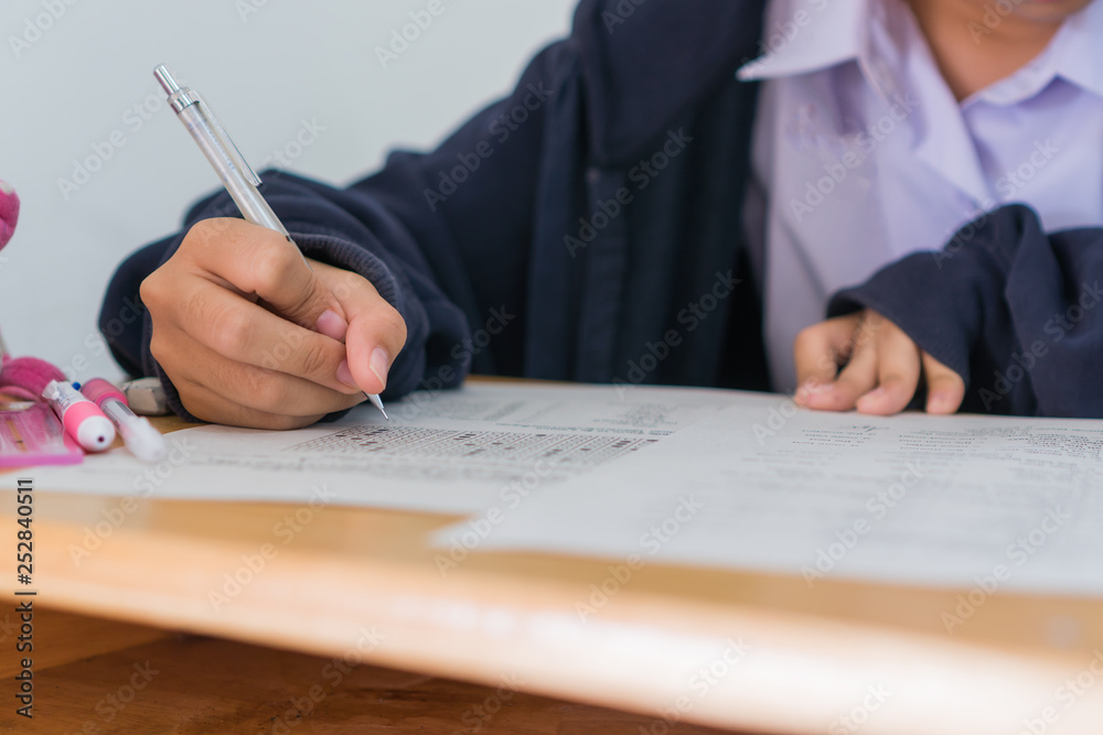 Exams test student in high school, university student holding pencil for testing exam writing answer sheet and exercise for taking in assessment paper on wood table classroom. Education study Concept Exams test student in high school, university student holding pencil for testing exam writing answer sheet and exercise for taking in assessment paper on wood table classroom. Education study Concept