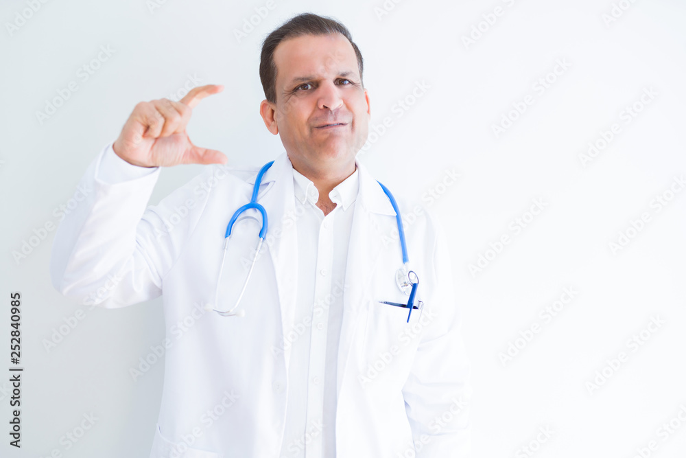 Middle age doctor man wearing stethoscope and medical coat over white background smiling and confident gesturing with hand doing size sign with fingers while looking and the camera. Measure concept.
