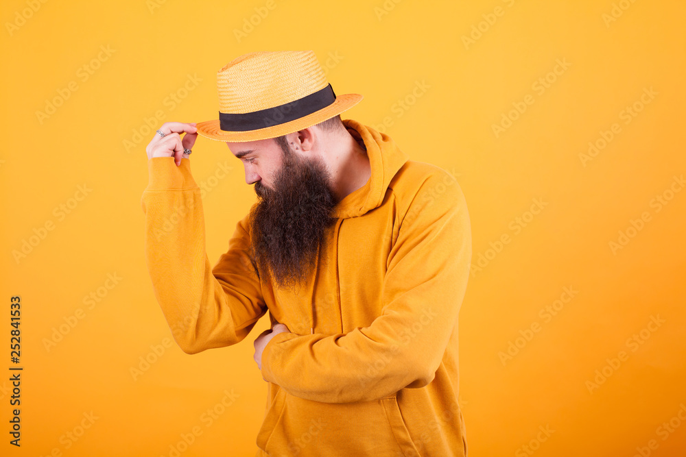Attractive bearded man touching his hat over yellow background Attractive bearded man touching his hat over yellow background