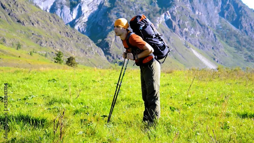 Hiking man walking on green mountain meadow with backpack. Summer sport and recreation concept. Hiking man walking on green mountain meadow with backpack. Summer sport and recreation concept.