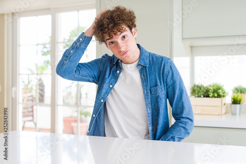 Young handsome man wearing casual denim jacket at home confuse and wonder about question. Uncertain with doubt, thinking with hand on head. Pensive concept. © Krakenimages.com