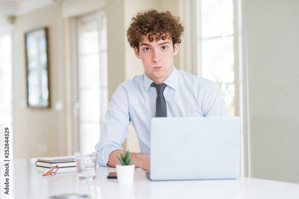 Young business man working with computer laptop at the office puffing cheeks with funny face. Mouth inflated with air, crazy expression.