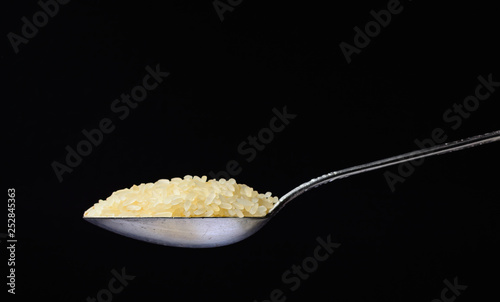 Raw rice poured into a silver spoon. Side view on a black background. Minimalism and space for text.