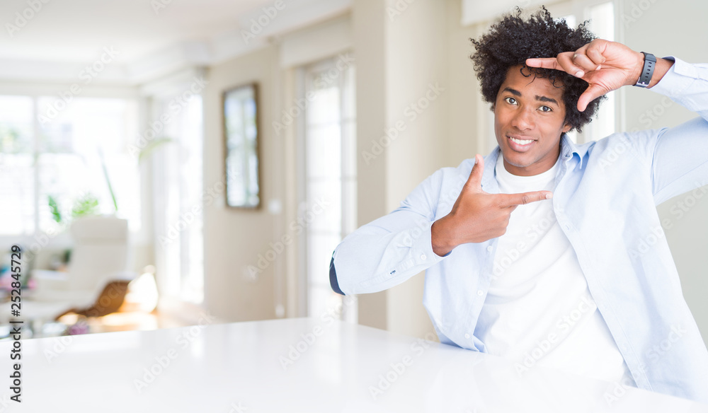 Obraz premium African American man at home smiling making frame with hands and fingers with happy face. Creativity and photography concept.