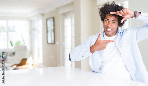 African American man at home smiling making frame with hands and fingers with happy face. Creativity and photography concept.