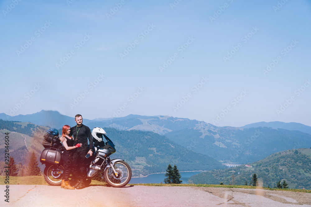 Young couple of motorcycle travelers enjoying a valley view in the top  summer mountains of Ceahlau, Romania. Moto tourism and travellers lifestyle  traveling Europe, copy spase, lake Lzvorul Muntelui Stock Photo