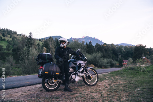 Rider Man and off tourism adventure motorcycles with side bags and equipment for long road trip  travel touring concept  Ceahlau  Romania  mountains on background  sunset evening