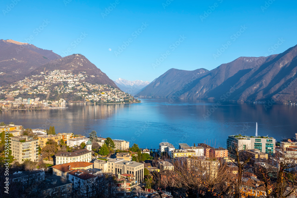 View over City and Alpine Lake Lugano with Mountain and the Moon in Switzerland.