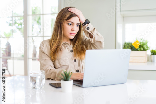 Beautiful young woman using computer laptop stressed with hand on head, shocked with shame and surprise face, angry and frustrated. Fear and upset for mistake.