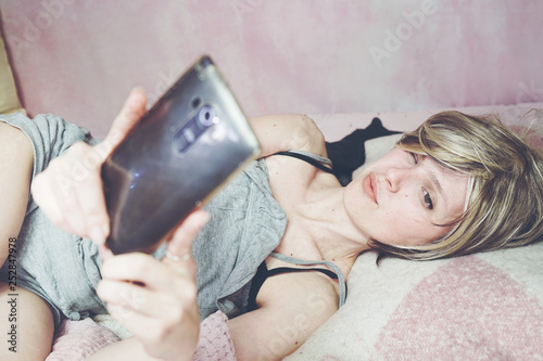 Young blond woman in her bed using her smart phone