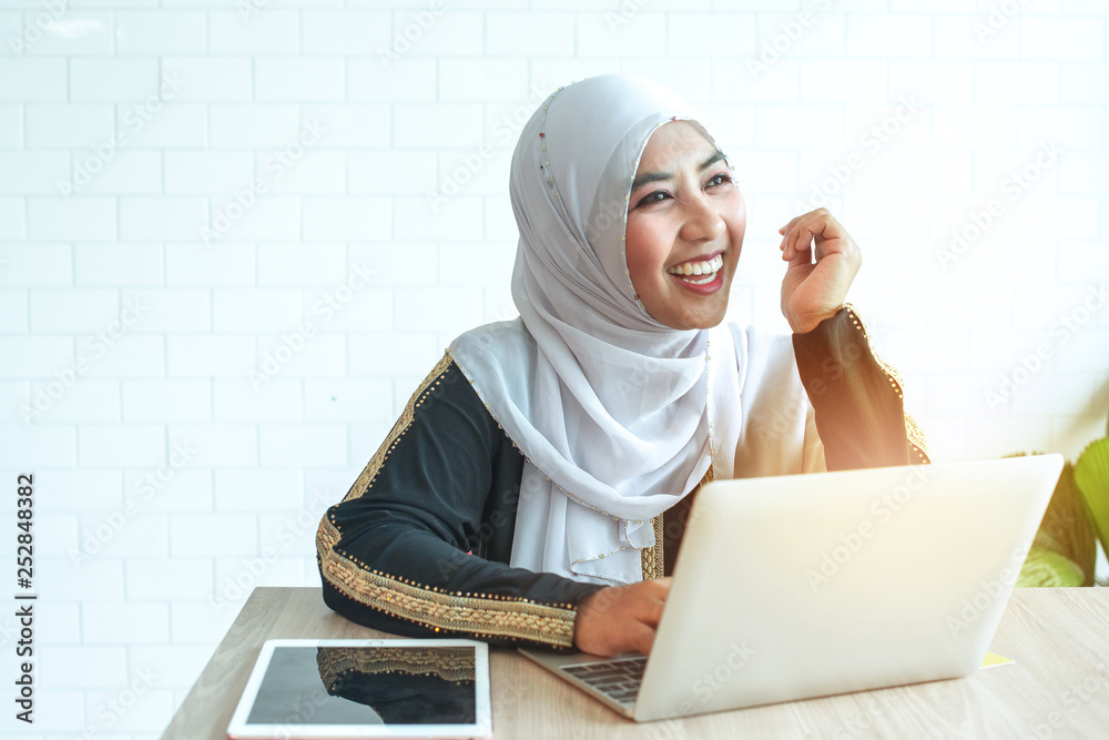 Portrait of cheerful Muslim business woman with tradition suit sitting at desk relaxing and smiling, happiness with her job, notebook computer in hand, Muslim concept Portrait of cheerful Muslim business woman with tradition suit sitting at desk relaxing and smiling, happiness with her job, notebook computer in hand, Muslim concept