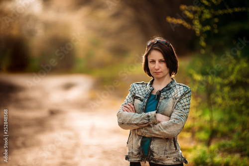 Photo of angry jealous middle-aged woman in blue jacket standing in spring forest with crossed hands
