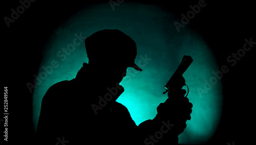 Fototapeta Naklejka Na Ścianę i Meble -  silhouette of a man with a gun in turquoise color spotlight in the darkness