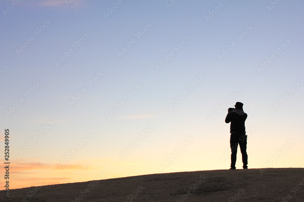 夕方の丘に立つカメラ男子のシルエット