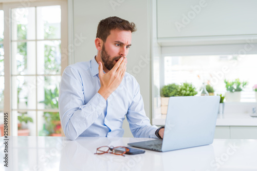 Handsome business man working using computer laptop cover mouth with hand shocked with shame for mistake, expression of fear, scared in silence, secret concept